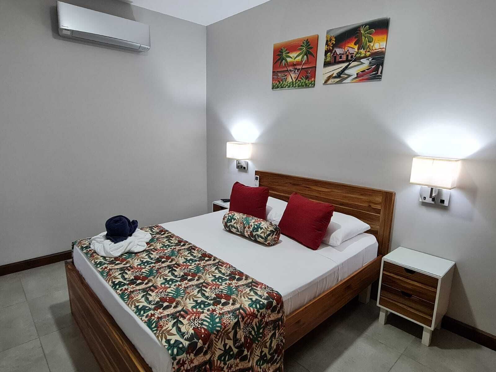 Une chambre d’hôtel comprenant un lit, deux lampes fixées au mur, une table de chevet et deux œuvres d’art décoratives.