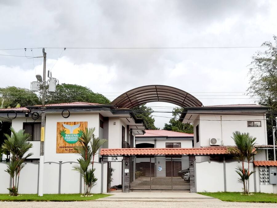 A two-story building with a red-tiled roof, a large sign advertising 'Ballena Paradise', and a gated entrance.