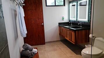 Un baño con tocador de madera, lavamanos, inodoro y espejo.