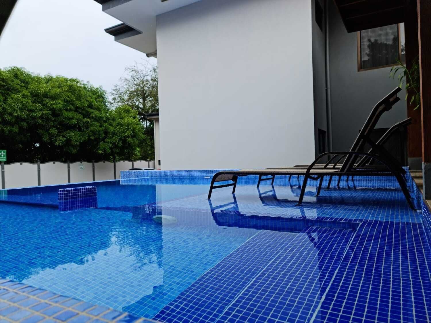 Una piscina exterior con agua cristalina azul, rodeada por un muro blanco y una terraza de madera.