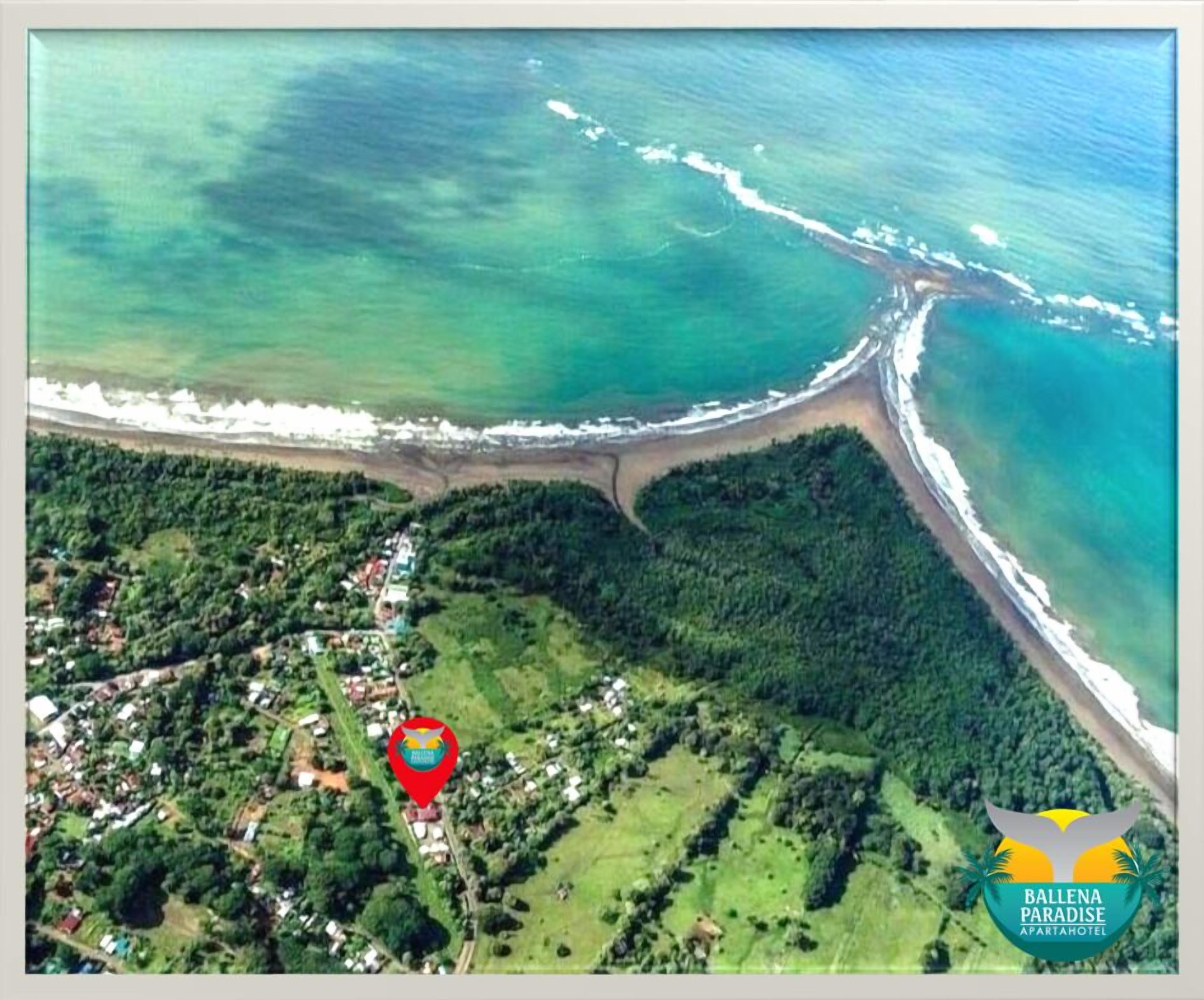 An aerial view of Ballena Paradise, featuring a coastal area with a beach, dense greenery, and a small cluster of buildings.