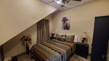 A bedroom with a bed, a ceiling fan, a wall-mounted lamp, and a painting.