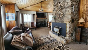 A cozy living room with a stone fireplace, leather sofa, and patterned rug. - Remodeled Historic Cabin (West Yellowstone)