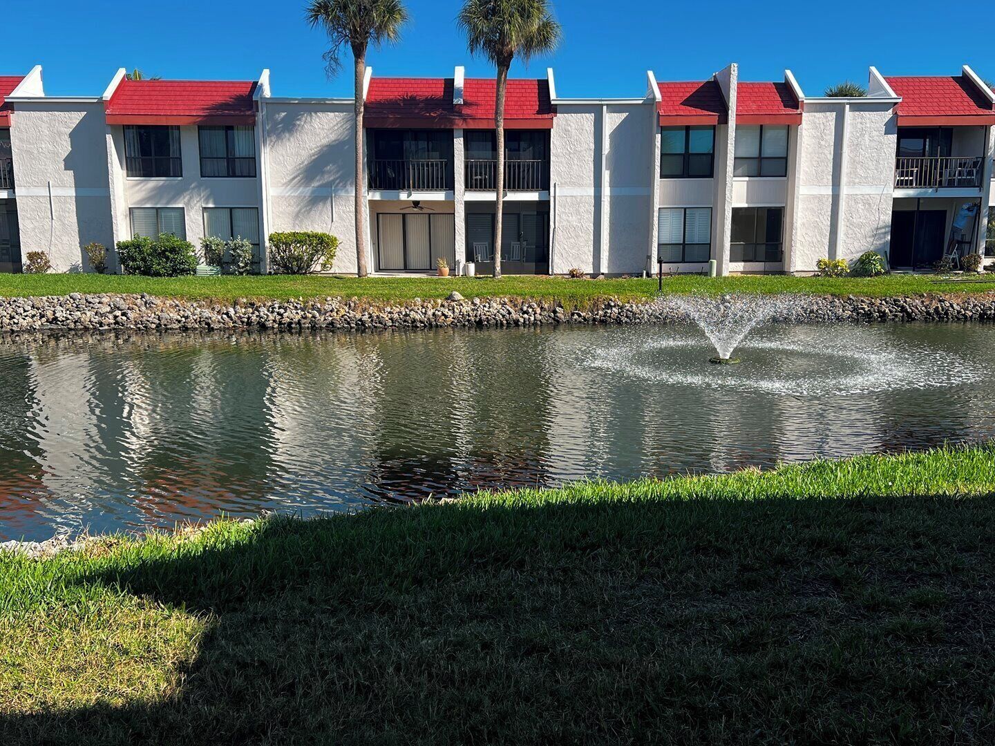 A modern building with a red roof, a small pond with a fountain, and a well-maintained lawn.