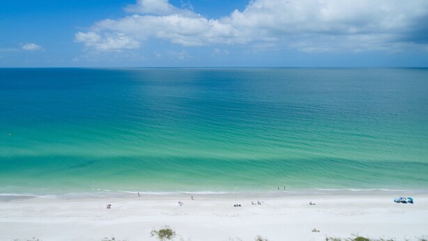A beach with clear turquoise water, white sand, and a few people and umbrellas. - Runaway Bay 107 - Beach, Pool, gym and much more (Unknown)