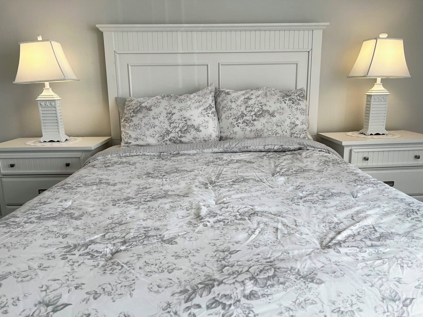 A bed with floral bedding, two bedside lamps, and a white headboard.
