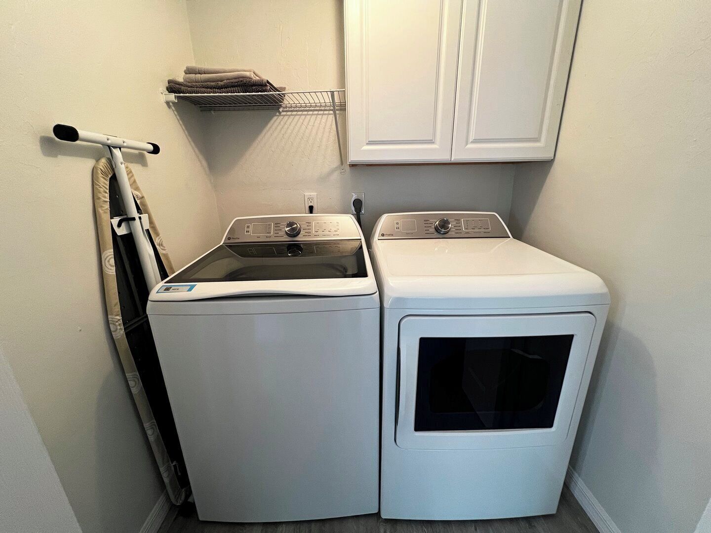 A laundry room with a front-loading washer and dryer, a drying rack, and a towel rack.