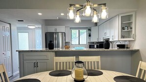 A modern kitchen with white cabinets, a stainless steel refrigerator, and a dining area with a round table and chairs. - Runaway Bay 107 - Beach, Pool, gym and much more (Unknown)
