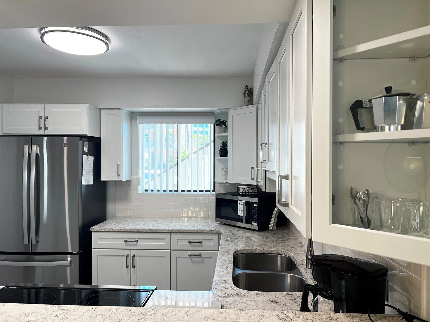 A modern kitchen with stainless steel appliances, white cabinetry, and a window with blinds.