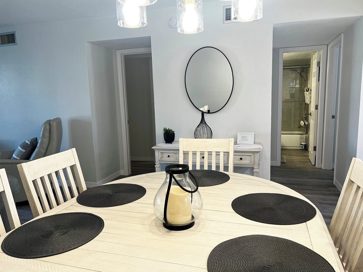 Un coin repas avec une table ronde, des sets de table noirs et un chandelier en guise de décoration centrale.