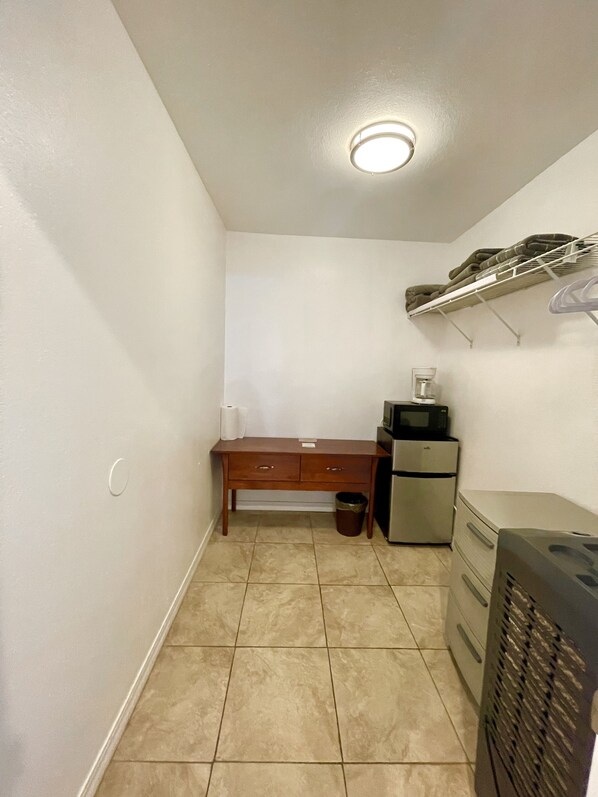 Una habitación pequeña y estrecha con un escritorio de madera, un bote de basura, un refrigerador y un calentador.