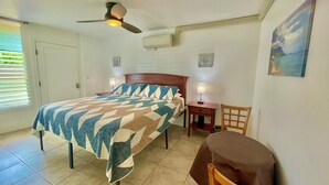 A bedroom with a bed, a nightstand, a chair, a ceiling fan, and a painting on the wall. - Beautiful Studio By The Beach! 1BR (Kapaʻa)