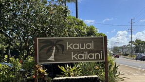 A sign for 'kauai kailani' with a tropical palm graphic, surrounded by greenery and a clear sky. - Beautiful Studio By The Beach! 1BR (Kapaʻa)