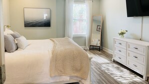 Une chambre à coucher avec un lit, un grand miroir, une commode et un téléviseur fixé au mur.