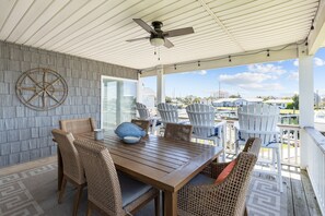 Un espace extérieur abrité, aménagé pour les repas, avec des meubles en osier, une table en bois et un ventilateur de plafond.