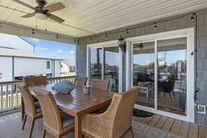 Une terrasse couverte avec une table en bois et des chaises en osier, de grandes portes-fenêtres coulissantes et un ventilateur de plafond.