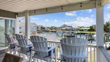 Une terrasse couverte, dotée de chaises Adirondack blanches, offre une vue sur une marina et ses bateaux.