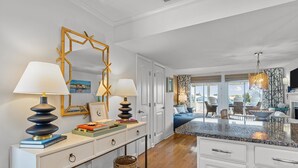 Cocina moderna con muebles blancos, encimera de granito y comedor con sofá azul y sillas de mimbre.