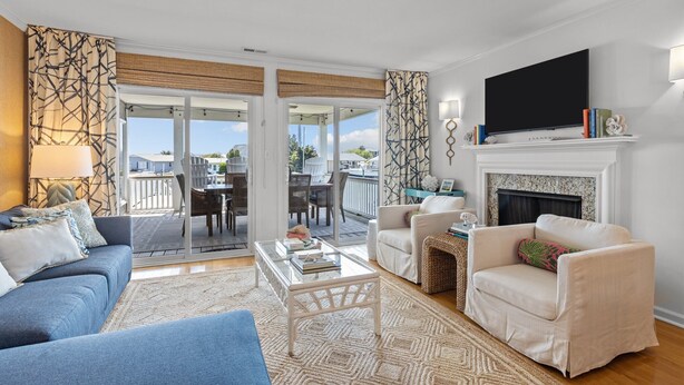 Una sala de estar con sofá, sillón, mesa de centro, chimenea, televisor y balcón con mobiliario exterior.