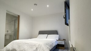 A bedroom with a bed, a bedside table, a wall-mounted TV, and a radiator. - Luxury 2-bed Apartment in Manchester With Parking (Salford)