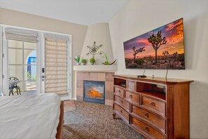 Um quarto com uma cama, lareira, cómoda de madeira, pintura de uma paisagem desértica e uma porta que dá para uma área externa.