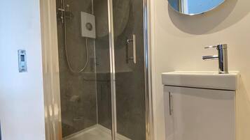 A modern bathroom with a glass-enclosed shower, a white sink, and a round mirror on the wall.