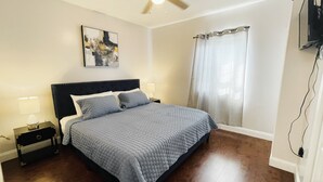 A bedroom with a bed, a nightstand, a ceiling fan, a painting, and a window with curtains. - Downtown of Pigeon Forge. Cozy 1 bed 1 bath condo <br>208 (Pigeon Forge)