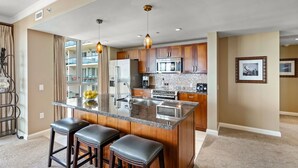 A modern kitchen with a central island, stainless steel appliances, and wooden cabinets. - Maui Resort Rentals: Honua Kai - 3 Total Bedrooms,  8th Floor "Penthouse" Ocean AND West Maui Mountain Views, Deluxe Corner Floor Plan! (Lahaina)