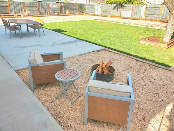 Eine Terrasse mit Tisch und zwei Holzstühlen, einem kleinen runden Tisch und einer Feuerstelle.