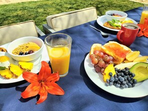 Ein Frühstückstisch im Freien mit Fruchtplatten, einem Orangensaftglas und einer roten Tasse.