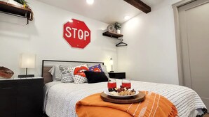 A neatly arranged bedroom with a bed, bedside tables, a wall-mounted stop sign, and a small shelf with a plant. - Comfortable, Laid-back Cottage. Private Yard. Near Zion. 2 Bedroom, Full Kitchen (Hurricane)