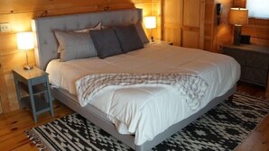 A wooden-paneled room with a bed, bedside tables, and wall decor. - Wild Peace  Secluded in Nature Fireplace, Pit (Waynesville)