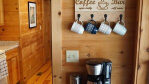 A cozy wooden cabin interior with a coffee bar, mugs hanging on hooks, and a coffee maker on the counter. - Wild Peace  Secluded in Nature Fireplace, Pit (Waynesville)
