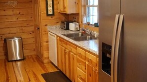 A wooden cabin-style kitchen with a stainless steel refrigerator, wooden cabinets, a sink, and a dishwasher. - Wild Peace  Secluded in Nature Fireplace, Pit (Waynesville)
