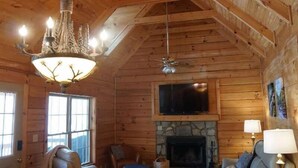 A log cabin interior with a chandelier, fireplace, television, and seating area. - Wild Peace  Secluded in Nature Fireplace, Pit (Waynesville)