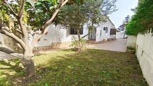 Un bâtiment blanc avec des fondations en pierre, une cour pavée et un arbre au premier plan.