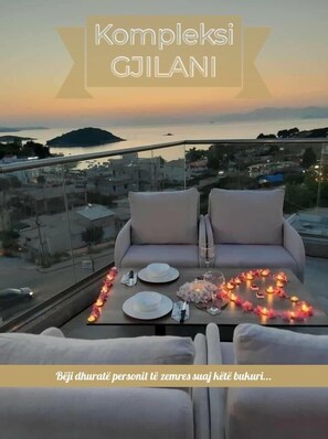 A balcony with a table set for two, overlooking a cityscape and water at sunset. - La Luna Resort Ksamil (Ksamil)