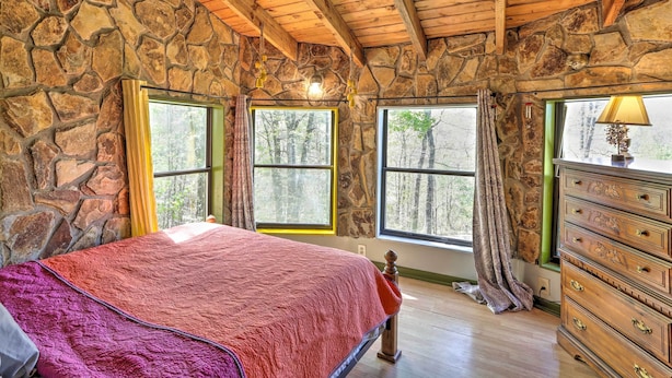A bedroom with stone walls, a wooden ceiling, a large bed, and a dresser with drawers.