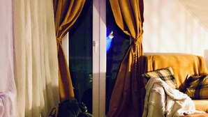 A room with a large window, curtains, a sofa with a plaid throw, and a visible night view outside. - Studio Sleeps 2 with Free Parking (Mexilhoeira Grande)
