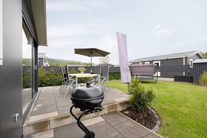 A patio with a grill, outdoor table, chairs, and a covered umbrella.