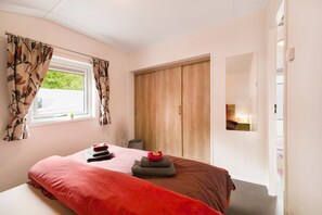 A bedroom with a bed, a window with curtains, a wooden wardrobe, and a mirror.