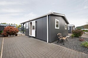 A small, modern building with a grey exterior, a bench, and a gravel area with plants.
