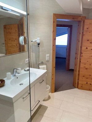 A bathroom with a glass shower enclosure, a white sink with a mirror, and wooden flooring. - Apartment 'W8 Haus Ganghofer' with Mountain View, Balcony & Wi-Fi (Leutasch)