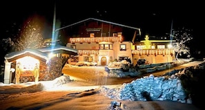 A hotel with a snow-covered entrance, a lit-up facade, and a Christmas tree. - Apartment 'W8 Haus Ganghofer' with Mountain View, Balcony & Wi-Fi (Leutasch)