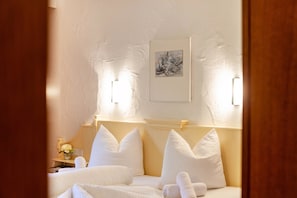 Habitación de hotel con cama, almohadas, mesita de noche, un florero con flores y un cuadro en la pared.