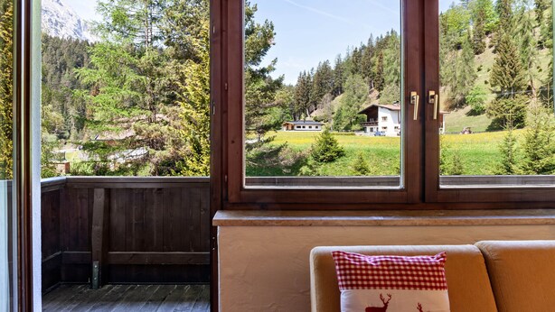 Une pièce dotée d’une terrasse en bois, de grandes fenêtres et d’un canapé agrémenté d’un coussin à carreaux.