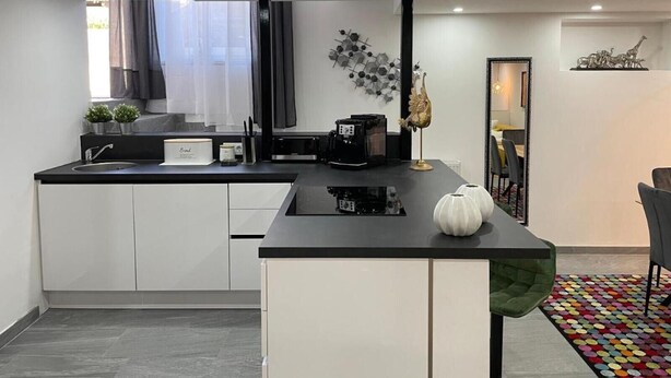 Una cocina moderna con encimera negra, armarios blancos, una cafetera y un adorno en la pared.