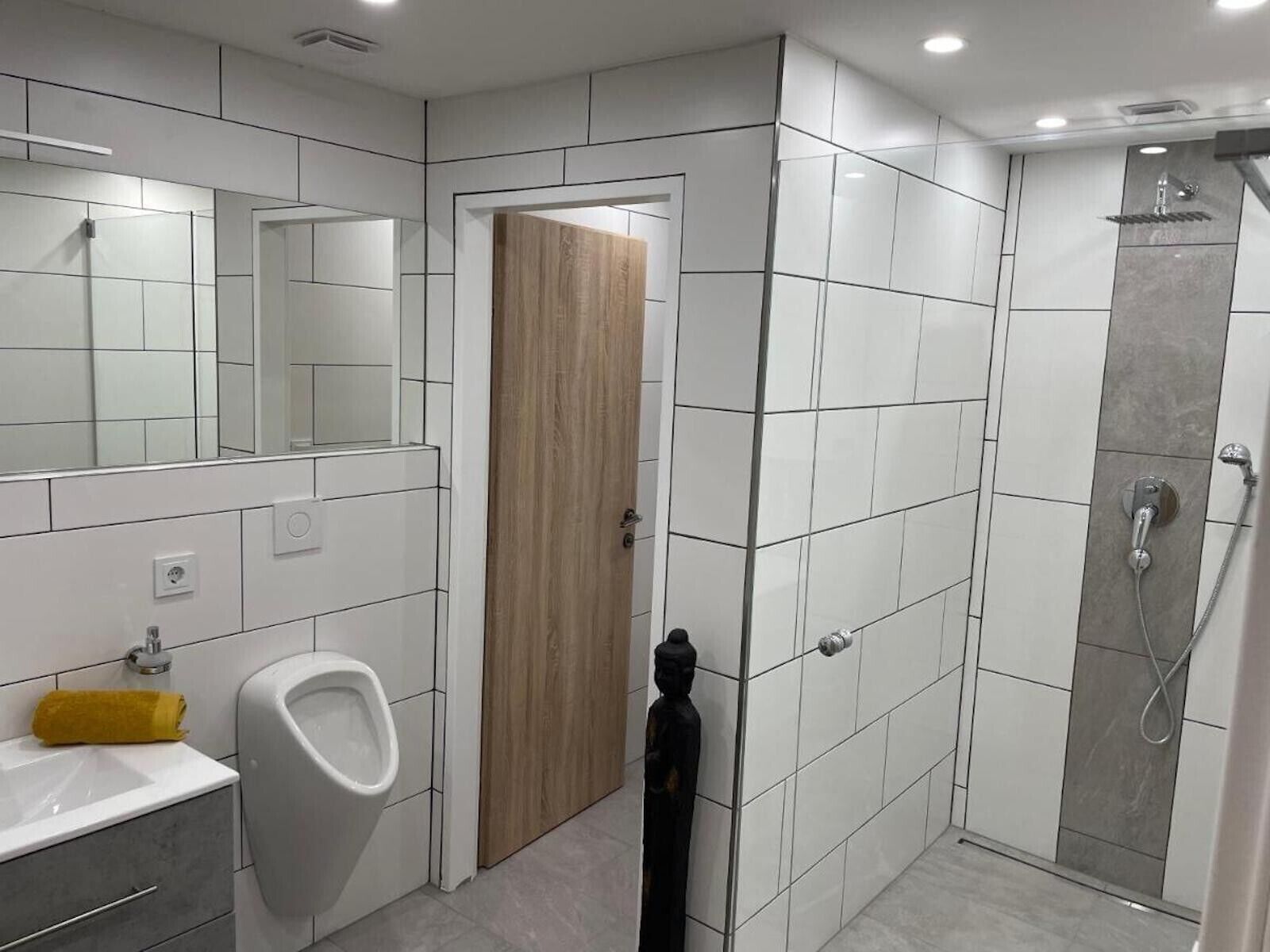 Un baño moderno con orinal, lavamanos, espejo y ducha.