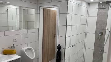 Un baño moderno con orinal, lavamanos, espejo y ducha.
