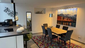 Un comedor moderno con una mesa de madera, sillas negras, un tapete colorido y un cuadro de un paisaje urbano en la pared.